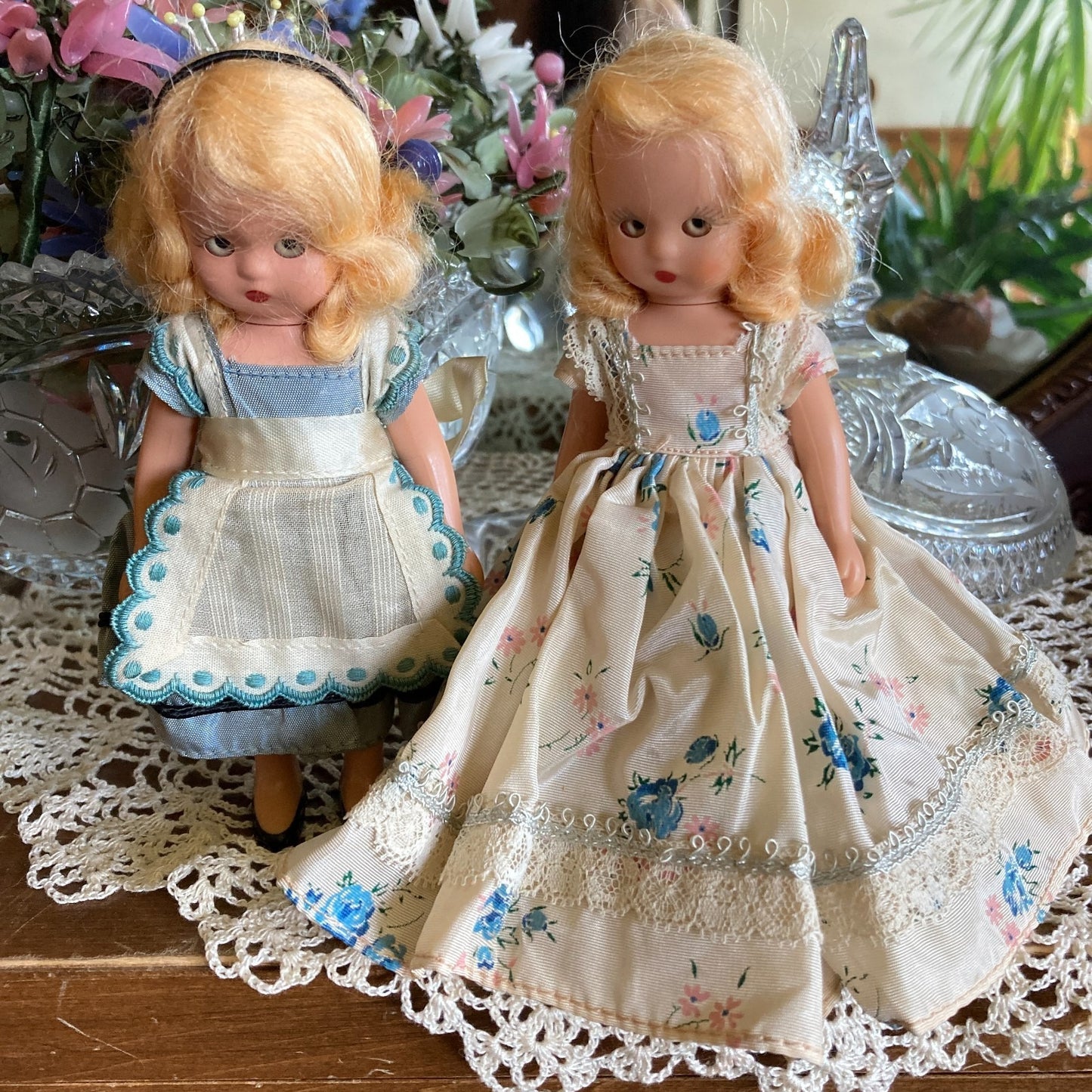 Two vintage dolls with dresses on a lace tablecloth.