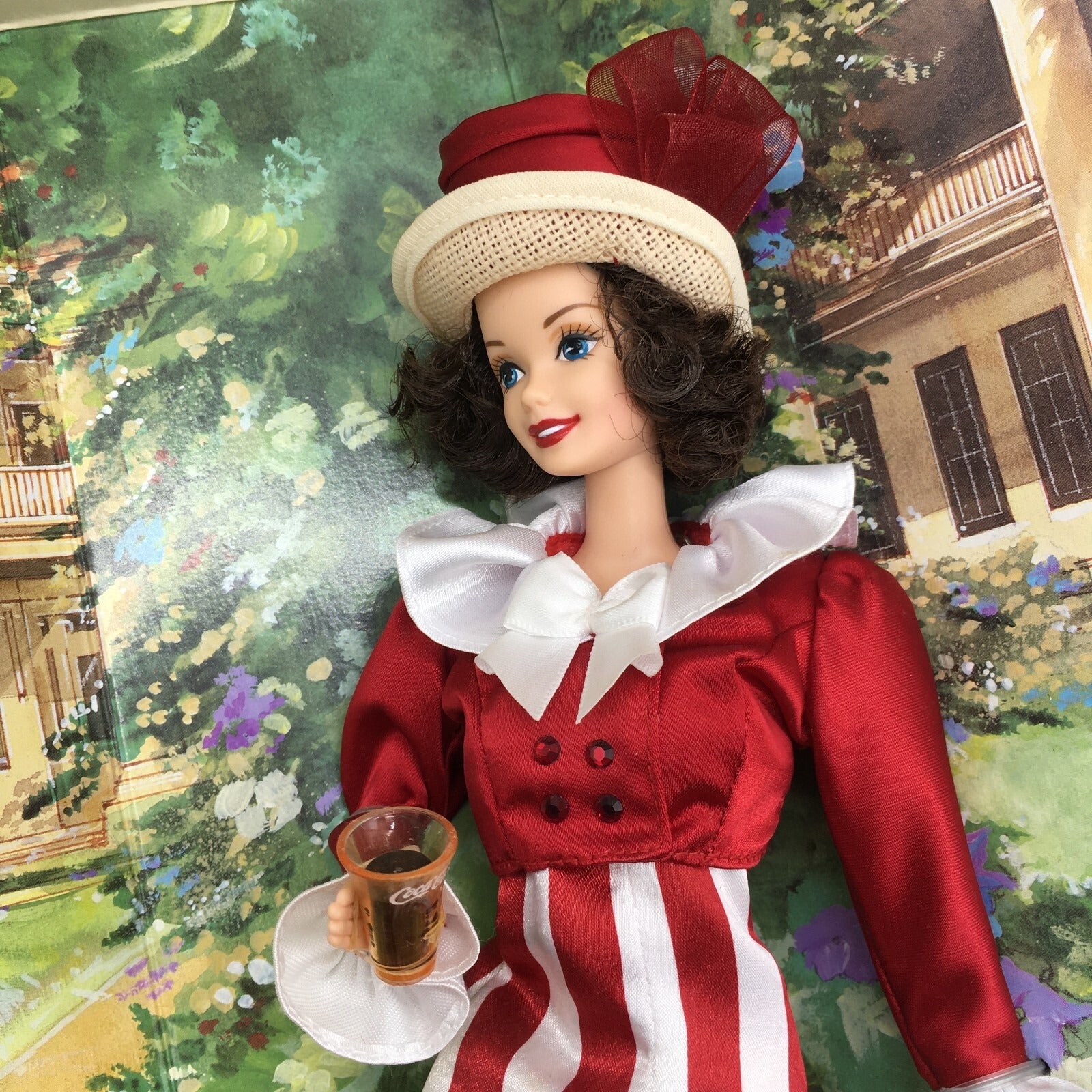 Barbie doll in a red and white outfit with a hat, holding a cup of Coca Cola, against a decorative background.