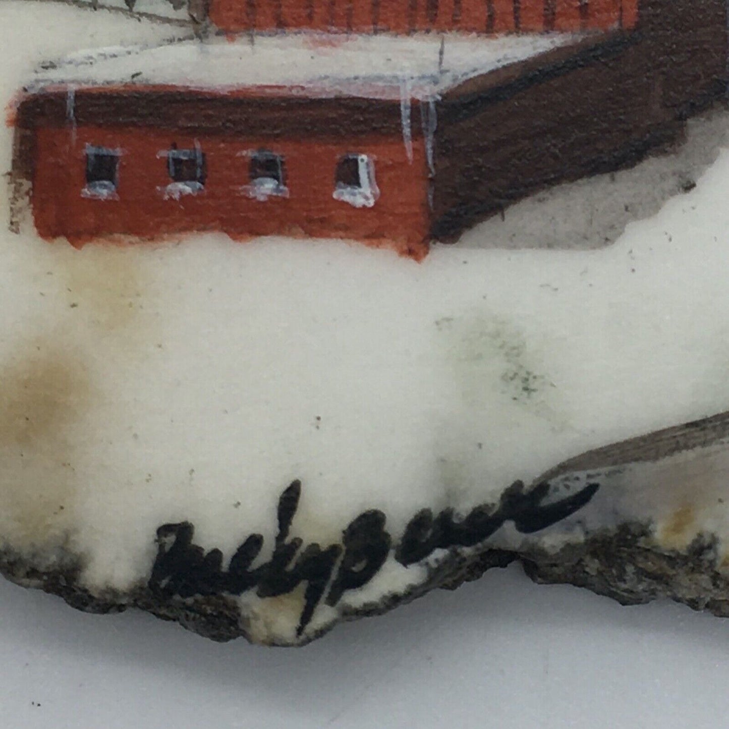 Close-up of a painted artwork showing part of a red building with snow on top, on a white surface with a black cursive signature near the bottom.