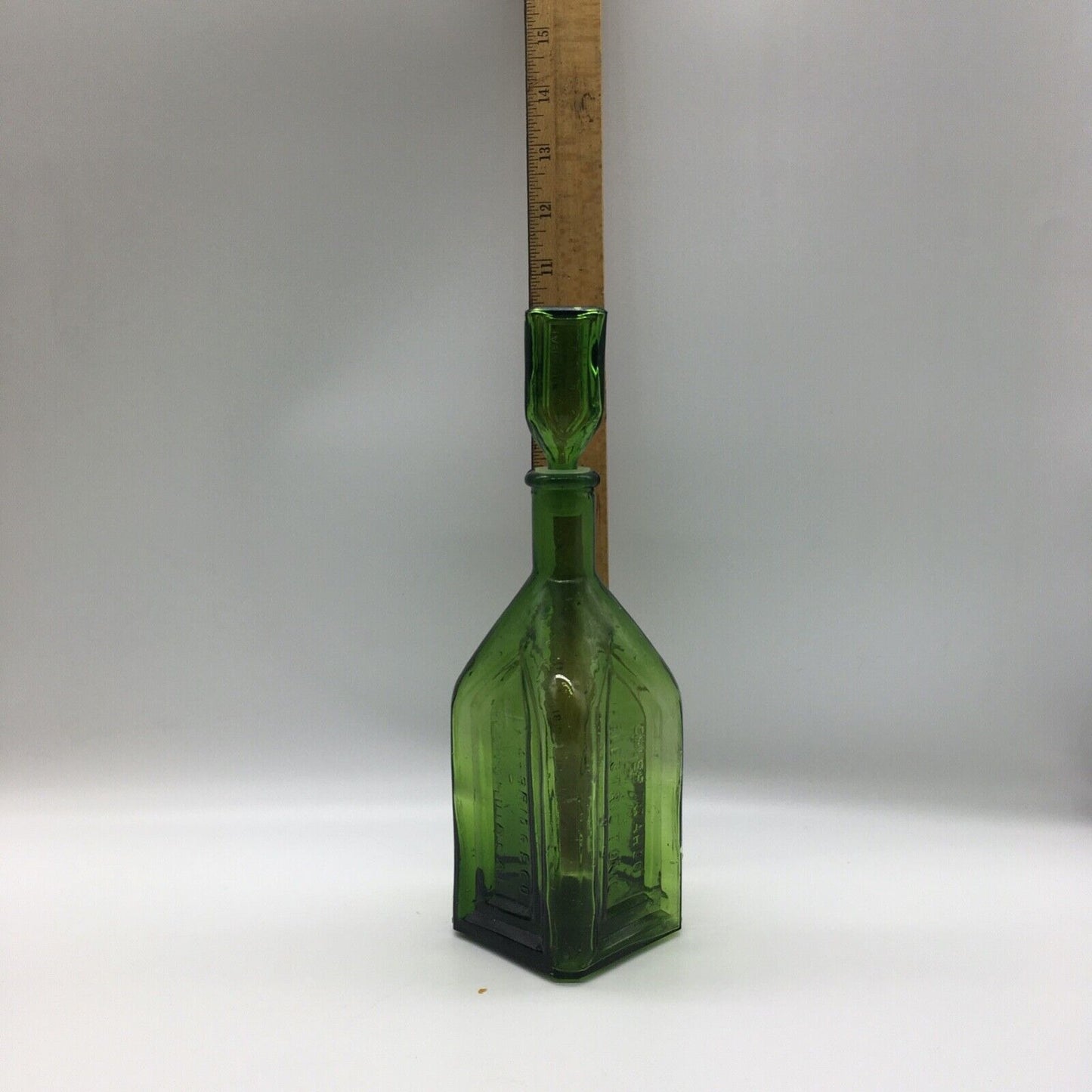 Green glass bottle with a wooden ruler for scale on a white background