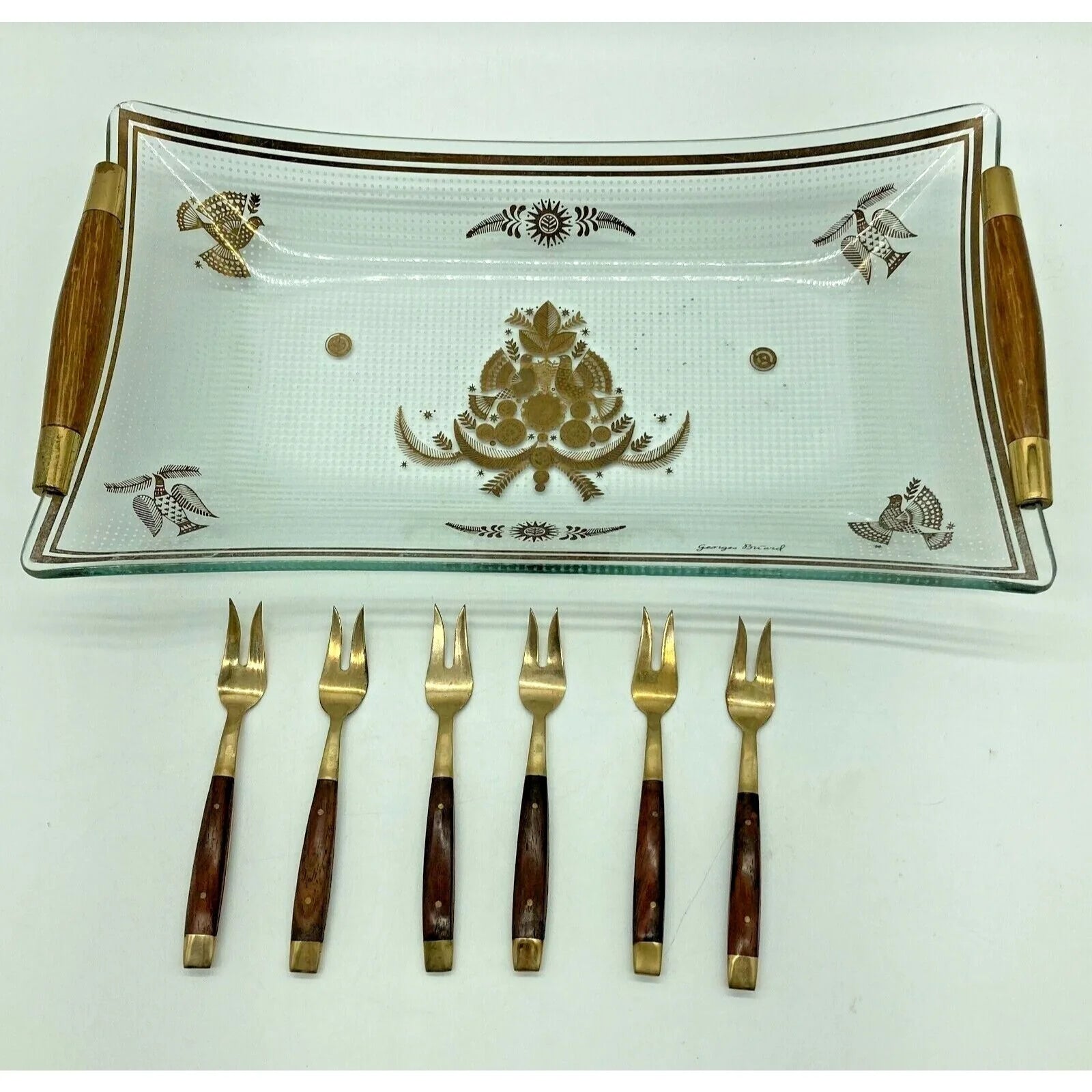 Decorative glass tray with gold patterns and six matching forks on a white background